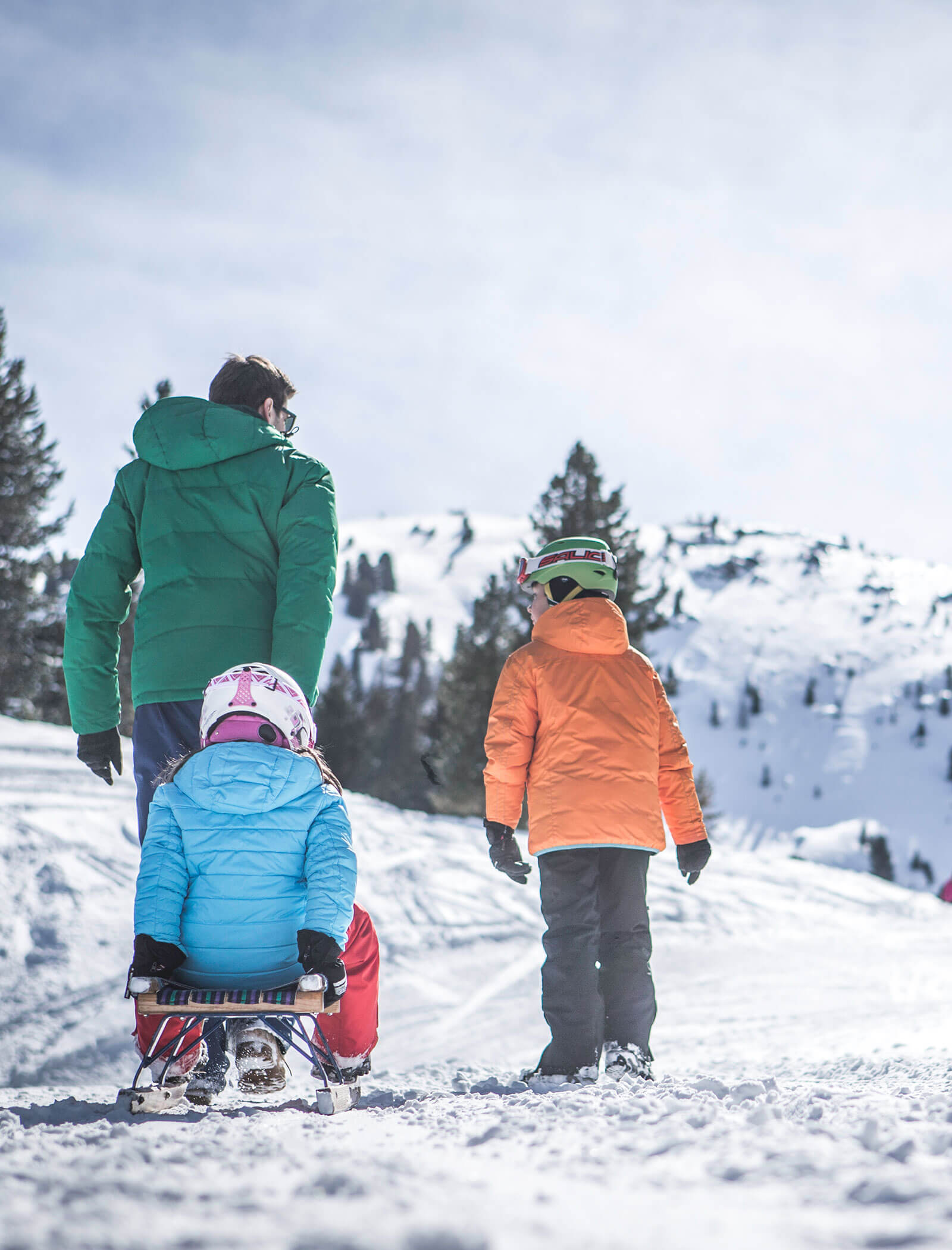 Ein Vater zieht seine Tochter die Rodelbahn hinauf und der Sohn geht daneben her - Hofer